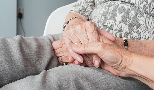 Eine Haushaltshilfe hält die Hand einer Seniorin, die im Sessel sitzt.