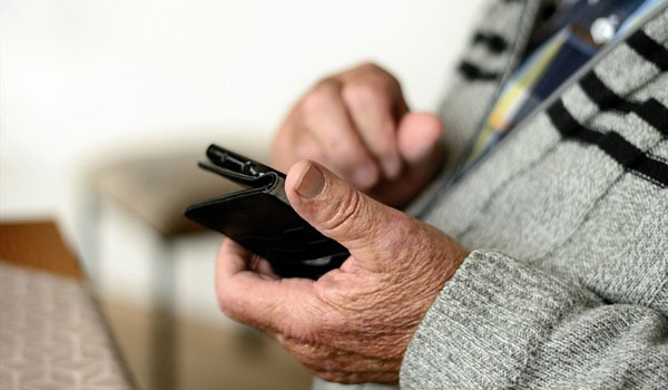 Ein Senior hat sein Handy in der Hand und überlegt ob er ein Foto schicken soll.