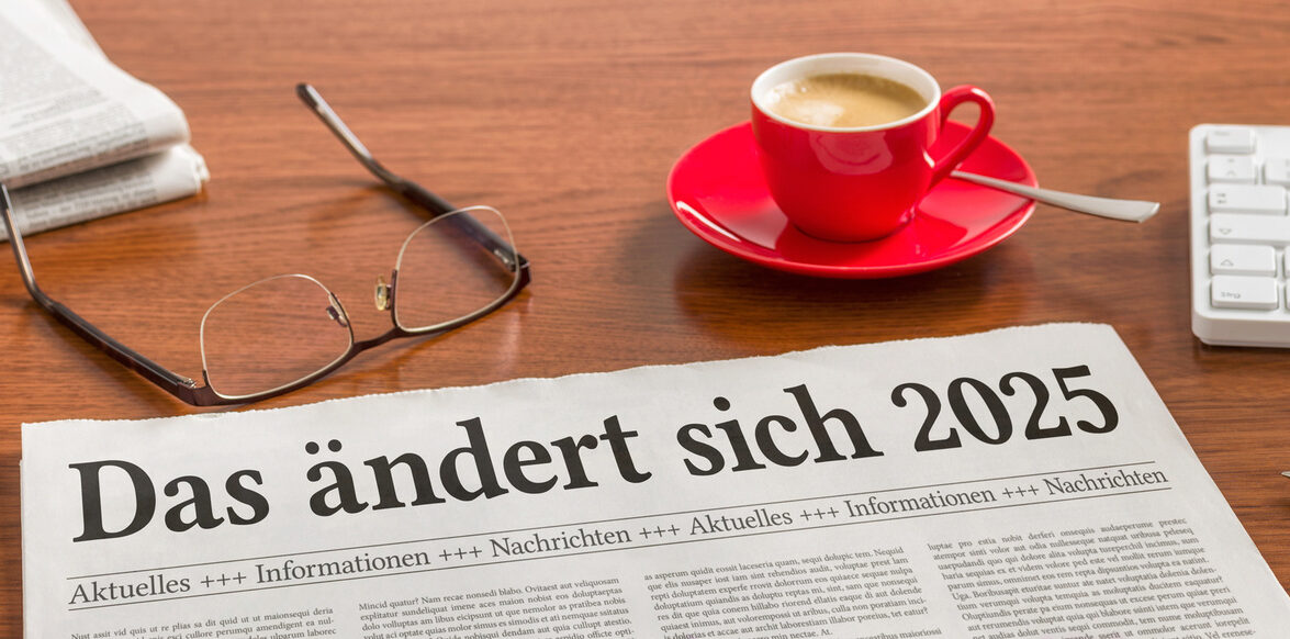 Auf einem Schreibtisch liegt eine Zeitung mit der Überschrift: "Das ändert sich 2025" dazu eine Tasse Espresso und eine Lesebrille.