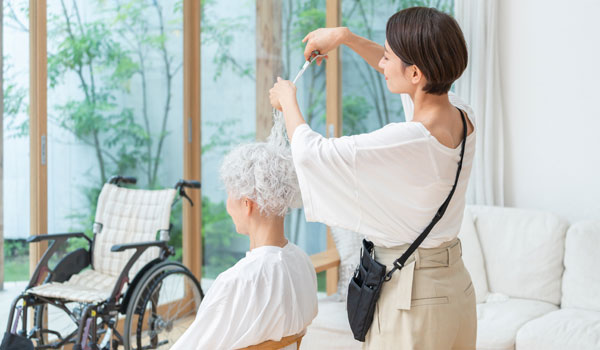 Eine Friseuse macht einer Seniorin die Haare in ihrem eigenem zu Hause.