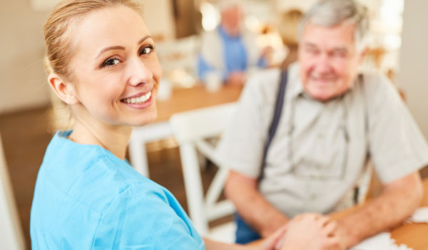 Eine Pflegedienst Mitarbeiterin besucht einen Senior bei sich zu Hause in der Küche.