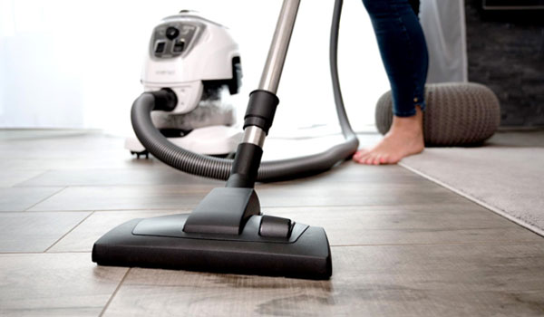 Eine Frau benutzt einen Staubsauger, um ihren Boden zu saugen. Es ist nur ihr Fuß zu sehen, 