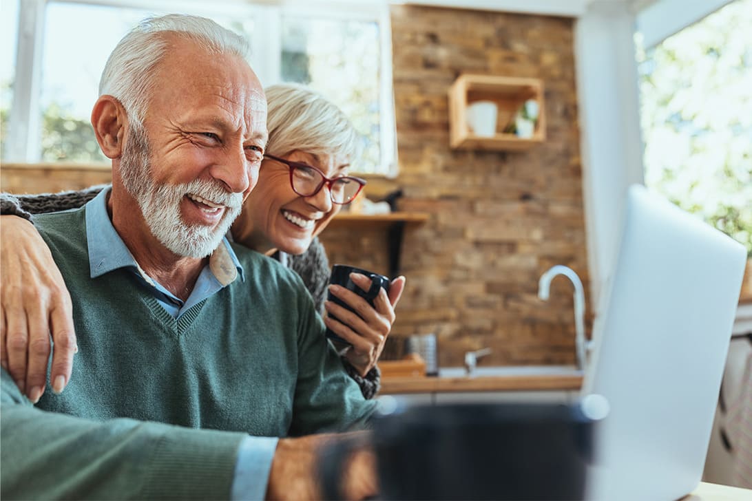 Ein Seniorenpaar sitzt vor seinem Laptop und freuen sich.