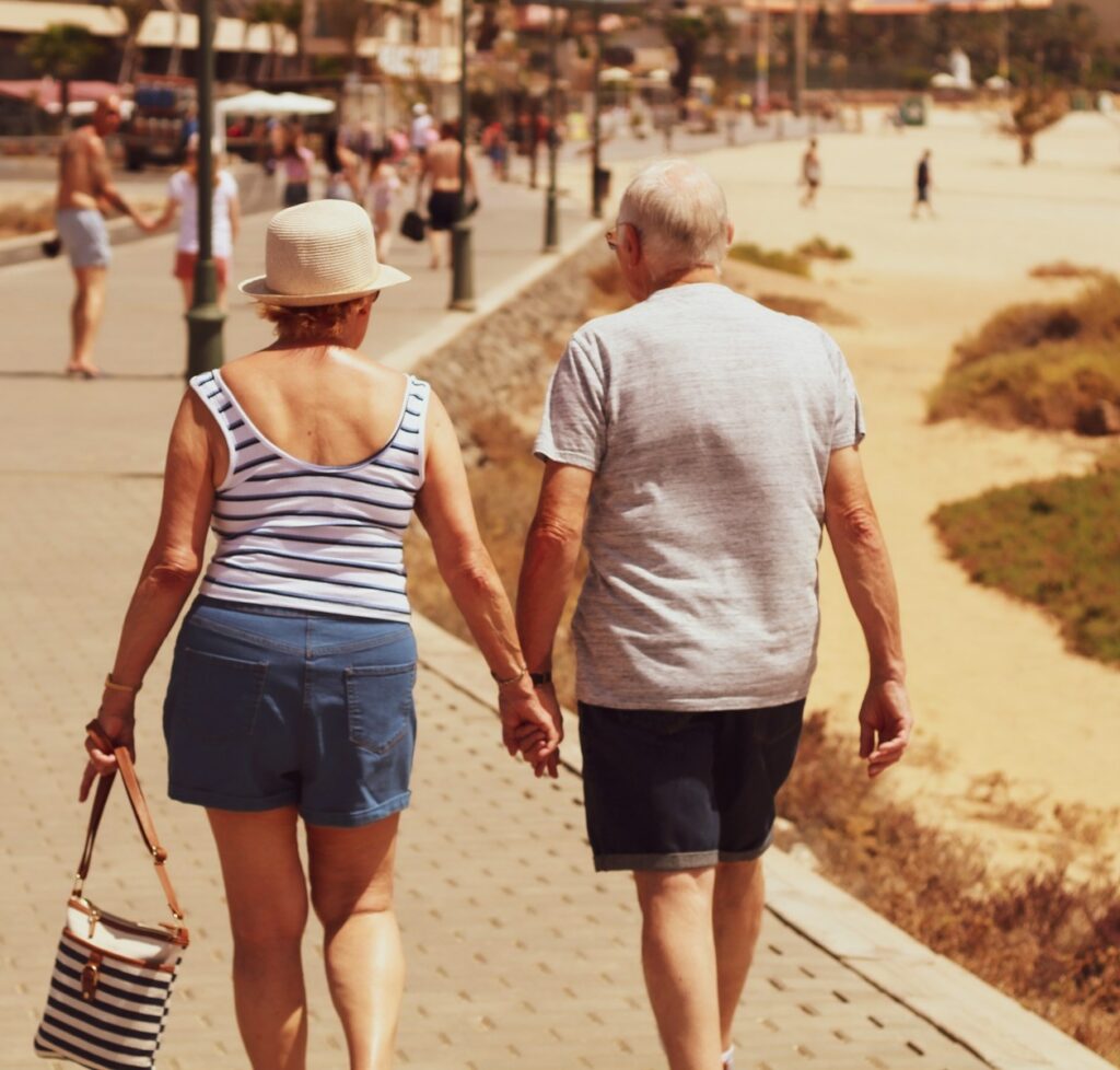 Älteres Paar hält Händchen und geht auf einem gepflasterten Weg am Strand entlang