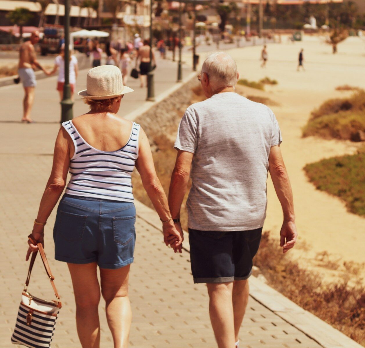 Älteres Paar hält Händchen und geht auf einem gepflasterten Weg am Strand entlang