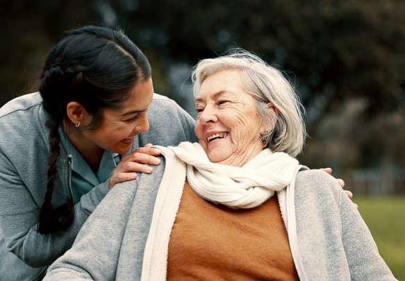 Eine Angehörige geht mit einer älteren Frau im Park spazieren.
