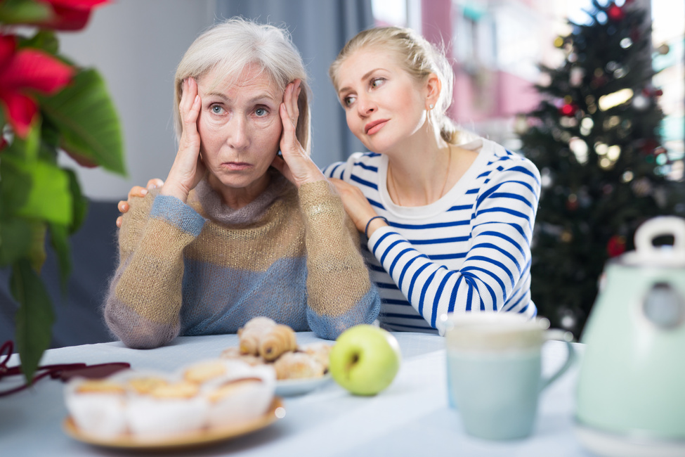 Erwachsene Tochter umarmt ihre unglückliche Mutter an Weihnachten.
