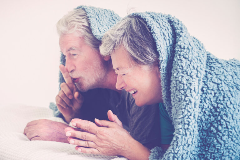 Liebe und Sexualität im Alter: ein älteres Paar hat Spass unter einer Bettdecke.
