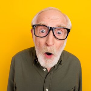 Ein Senior mit Hornbrille blickt erstaunt in die Kamera.