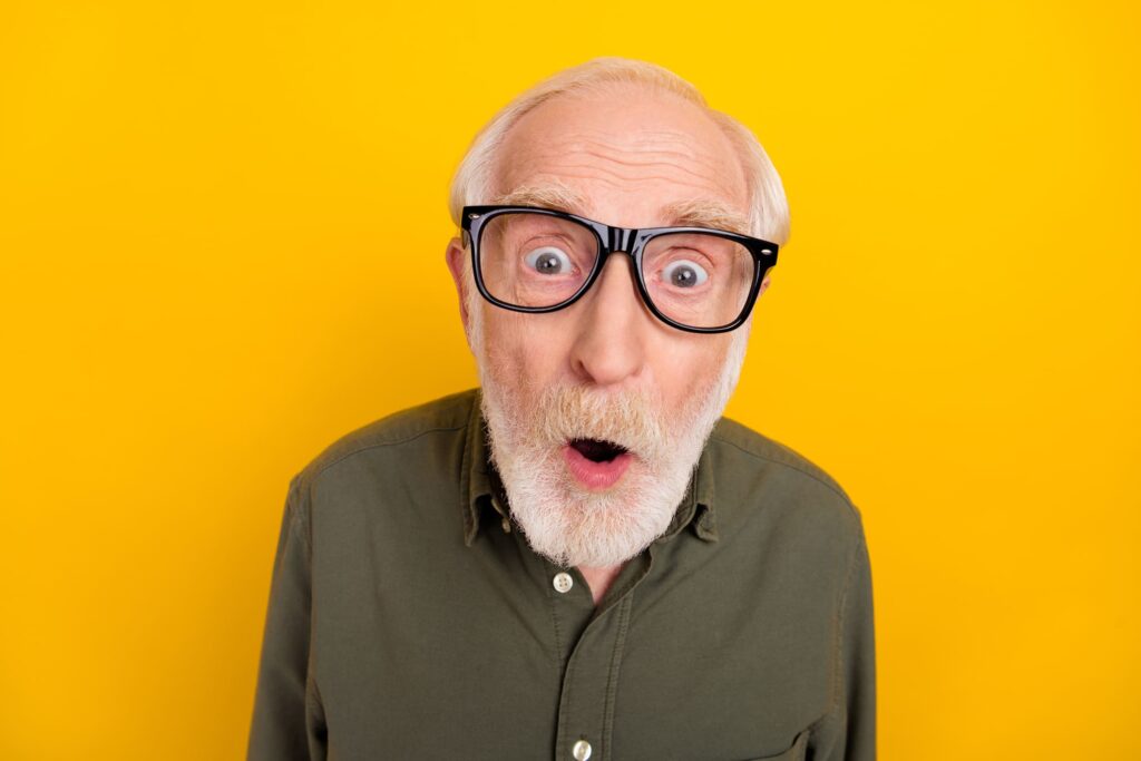 Ein Senior mit Hornbrille blickt erstaunt in die Kamera.